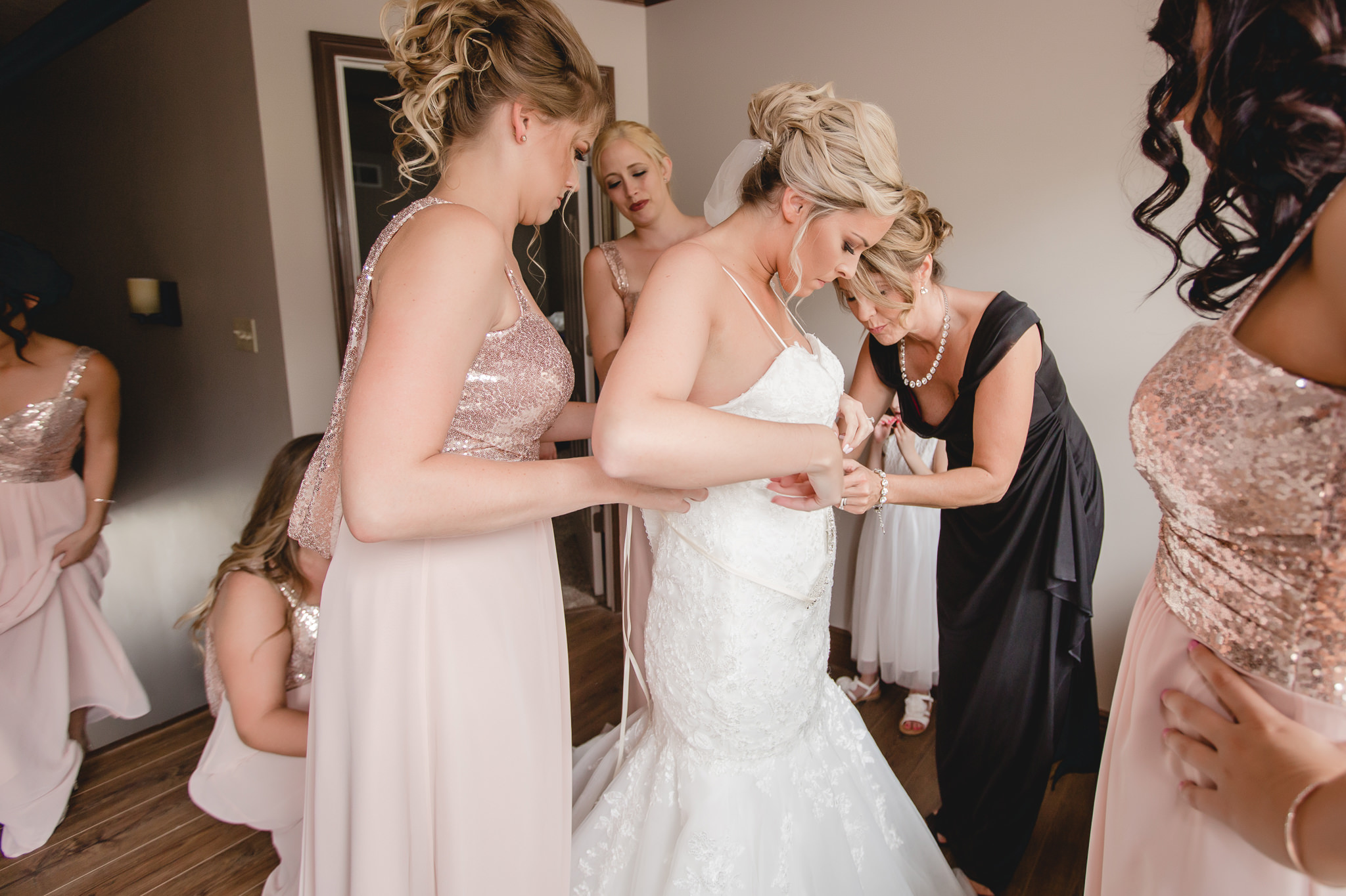 Mother of the bride and bridesmaids help the bride into her Alfred Angelo wedding dress