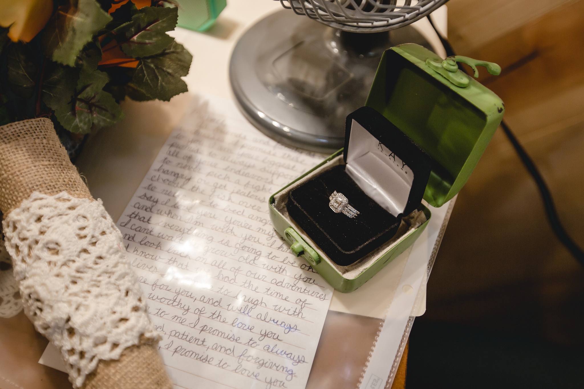 Bride's engagement ring in a vintage tin rests on her hand-written vows
