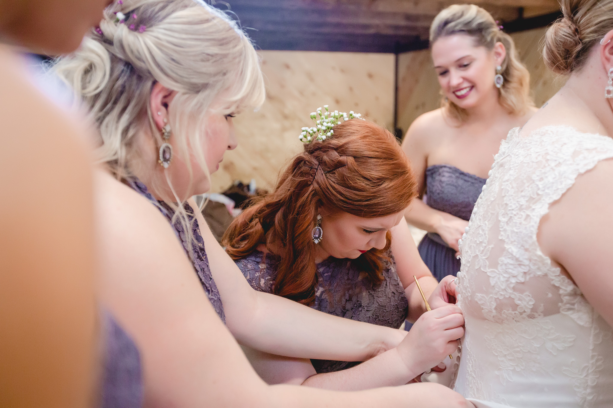 Maid of honor uses a crochet hook to button the bride's dress