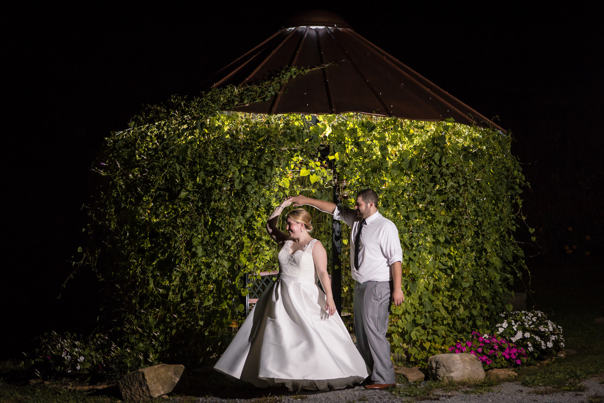 Groom twirls his bride at night in from of an ivy covered gazebo