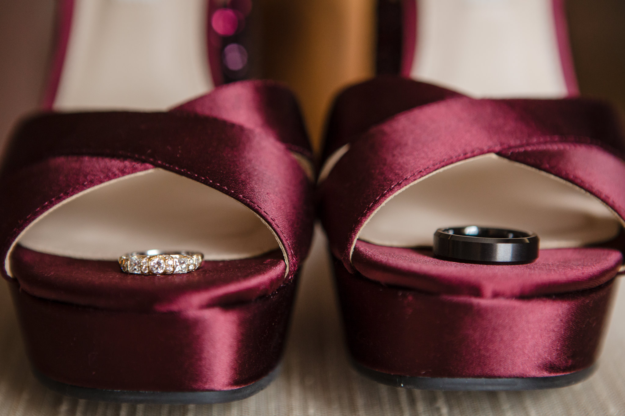 Wedding bands rest in the bride's burgundy shoes