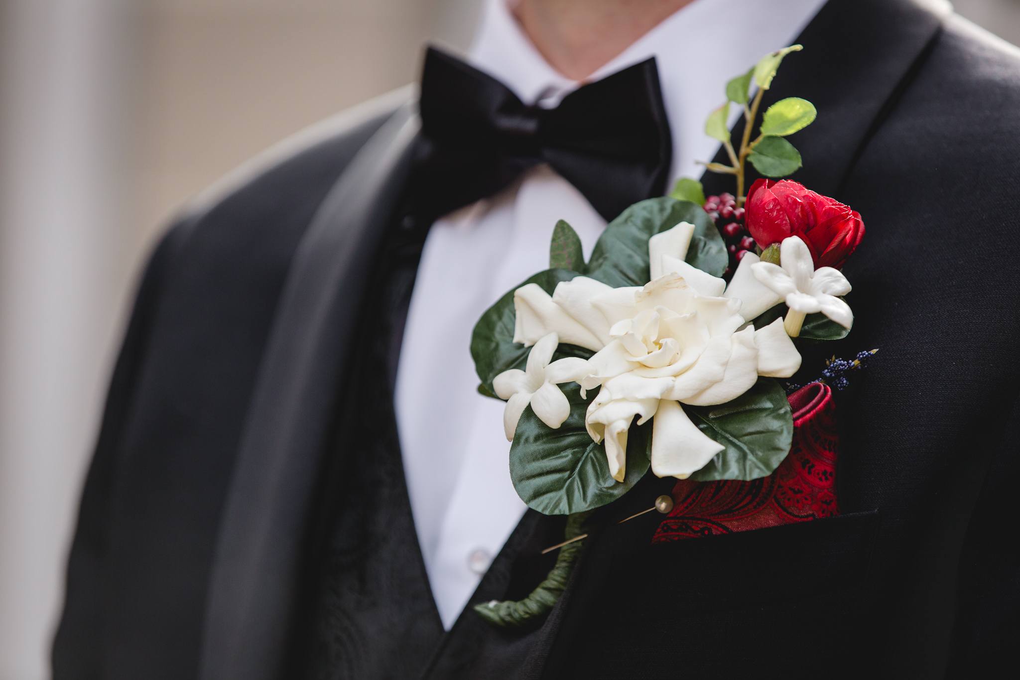 Close up of groom's boutonniere of white flowers and red accents