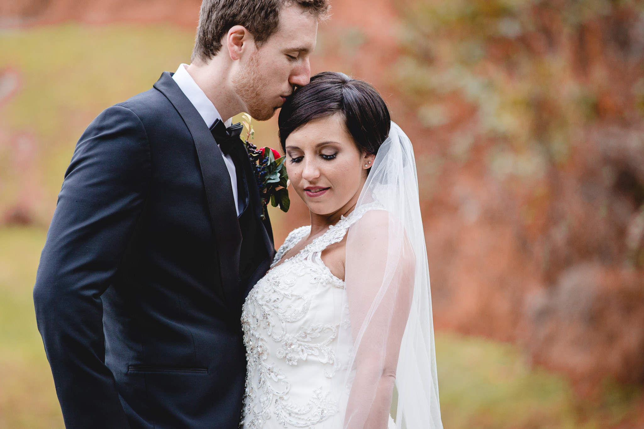 Groom kisses his bride's head during portraits for their fall wedding