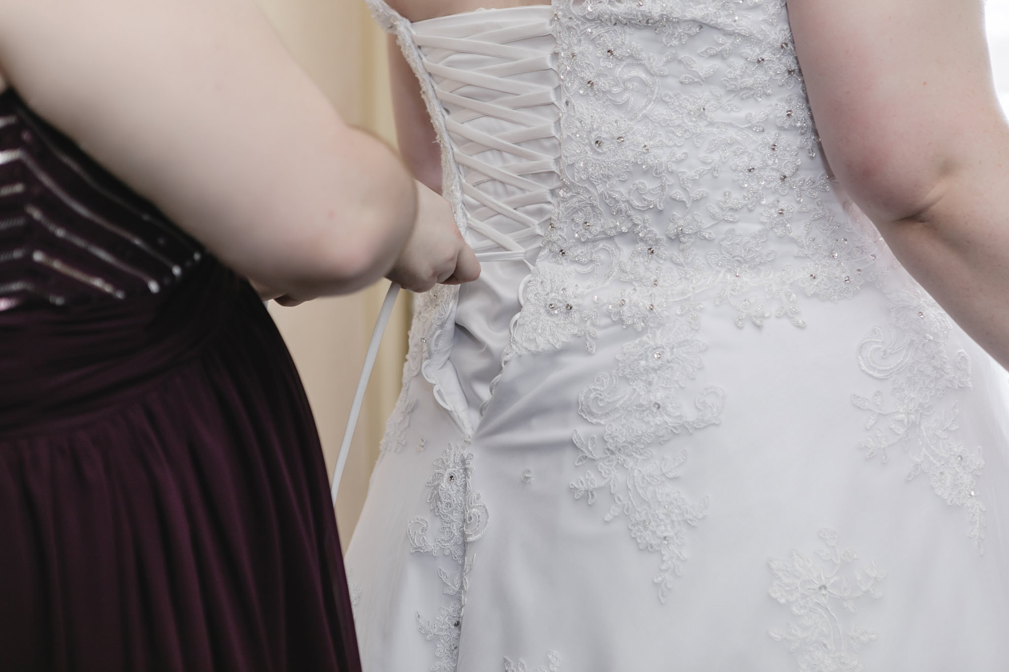 Maid of honor laces up bride's corset back wedding dress