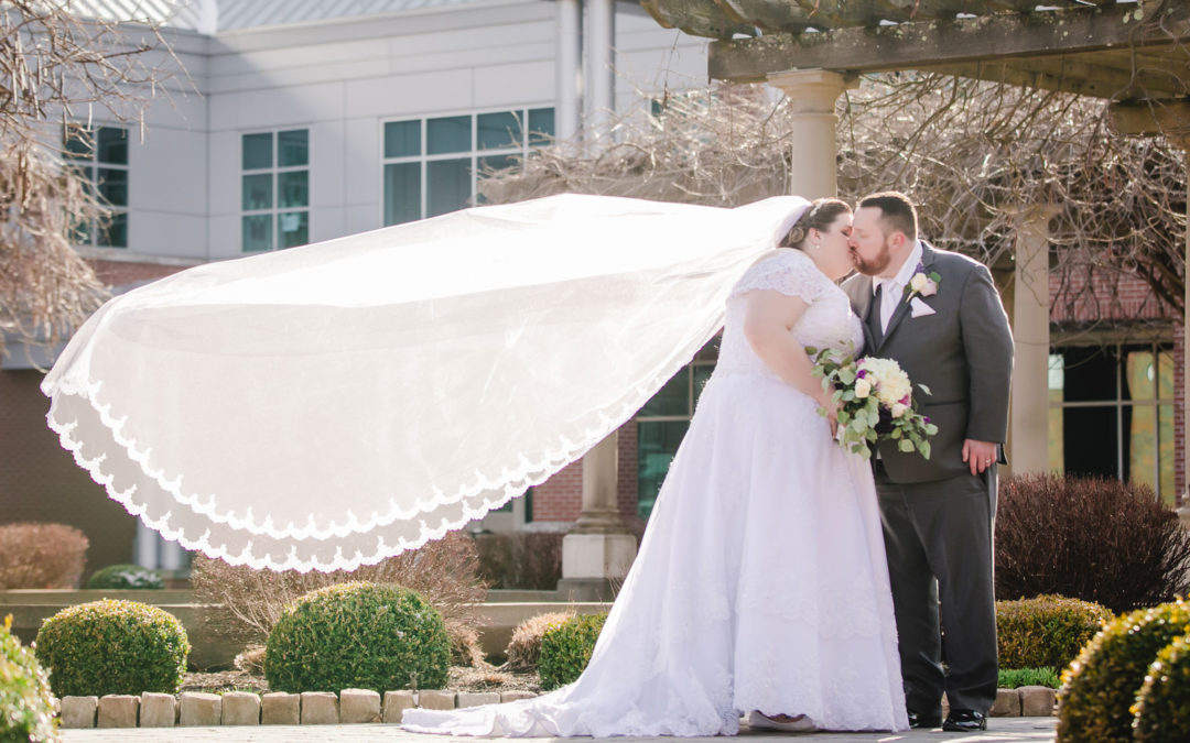Bride's cathedral veil floats behind her as she kisses her groom at Robert Morris University