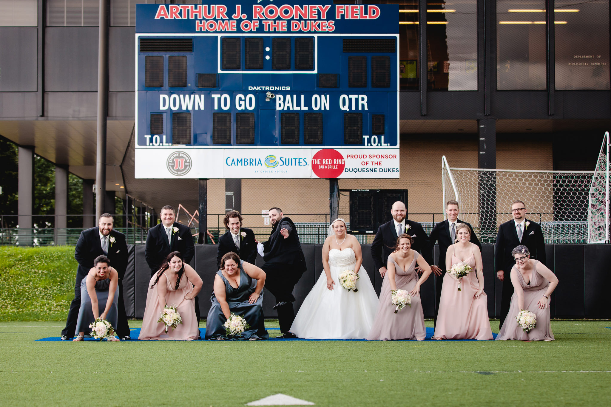 Bridal party poses as a football team on Duquesne University's Rooney Field