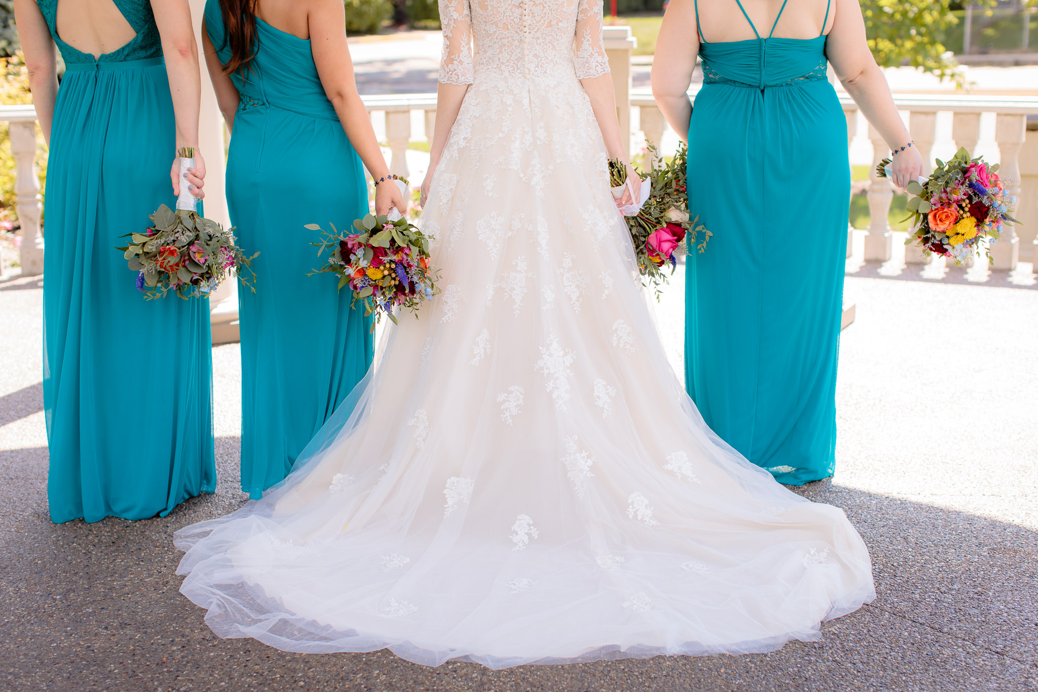 Bride's Maggie Sottero Bree wedding gown fanned out next to bridesmaids' turquoise dresses