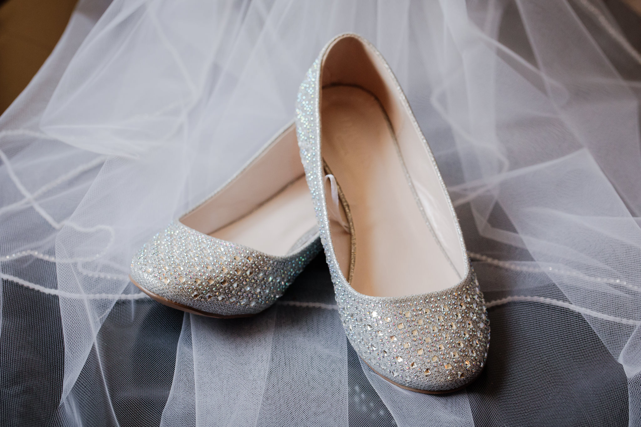Bride's silver flat wedding shoes sit on her white veil
