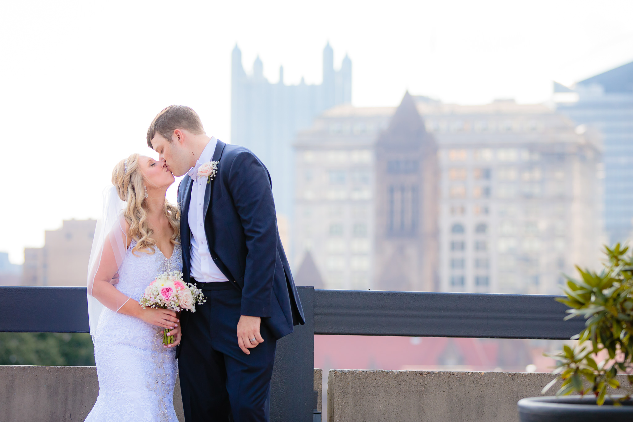 Newlyweds kiss in front of a downtown Pittsburgh backdrop at Duquesne University