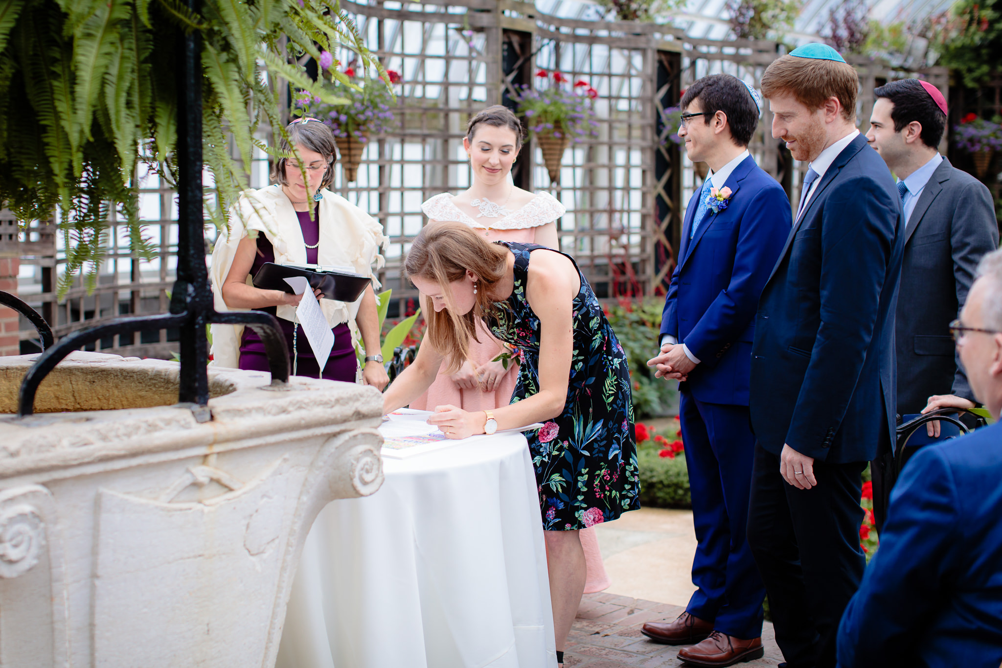 Bridal party & family looks on as female witness signs the Ketubah at Phipps Conservatory