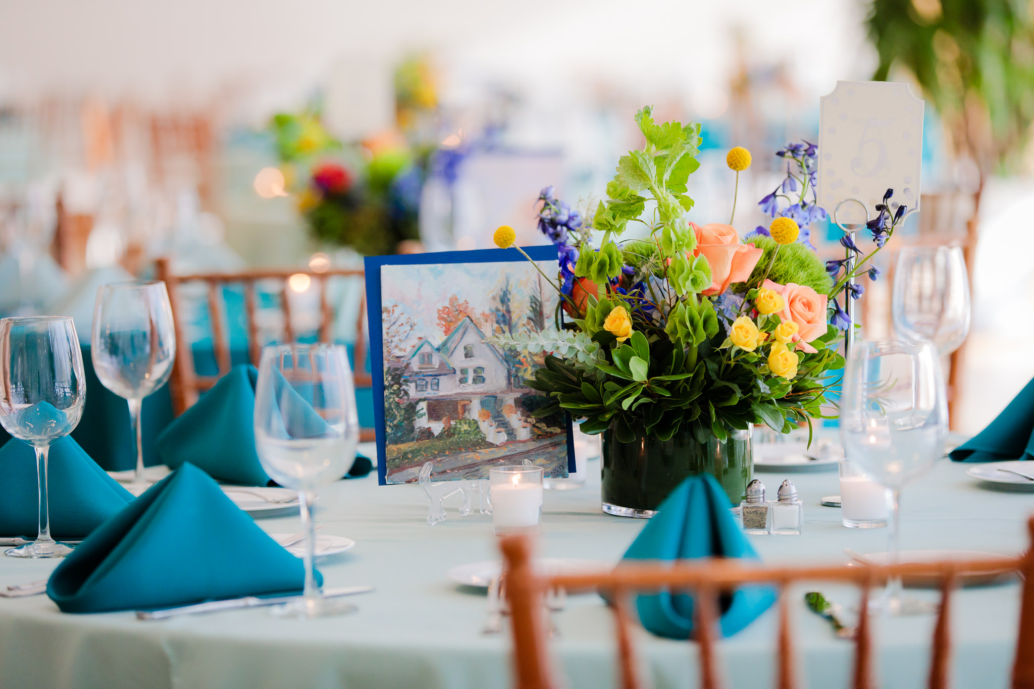 Floral centerpieces by Hepatica and a custom painting by the bride sit atop each table at a Phipps Conservatory wedding reception