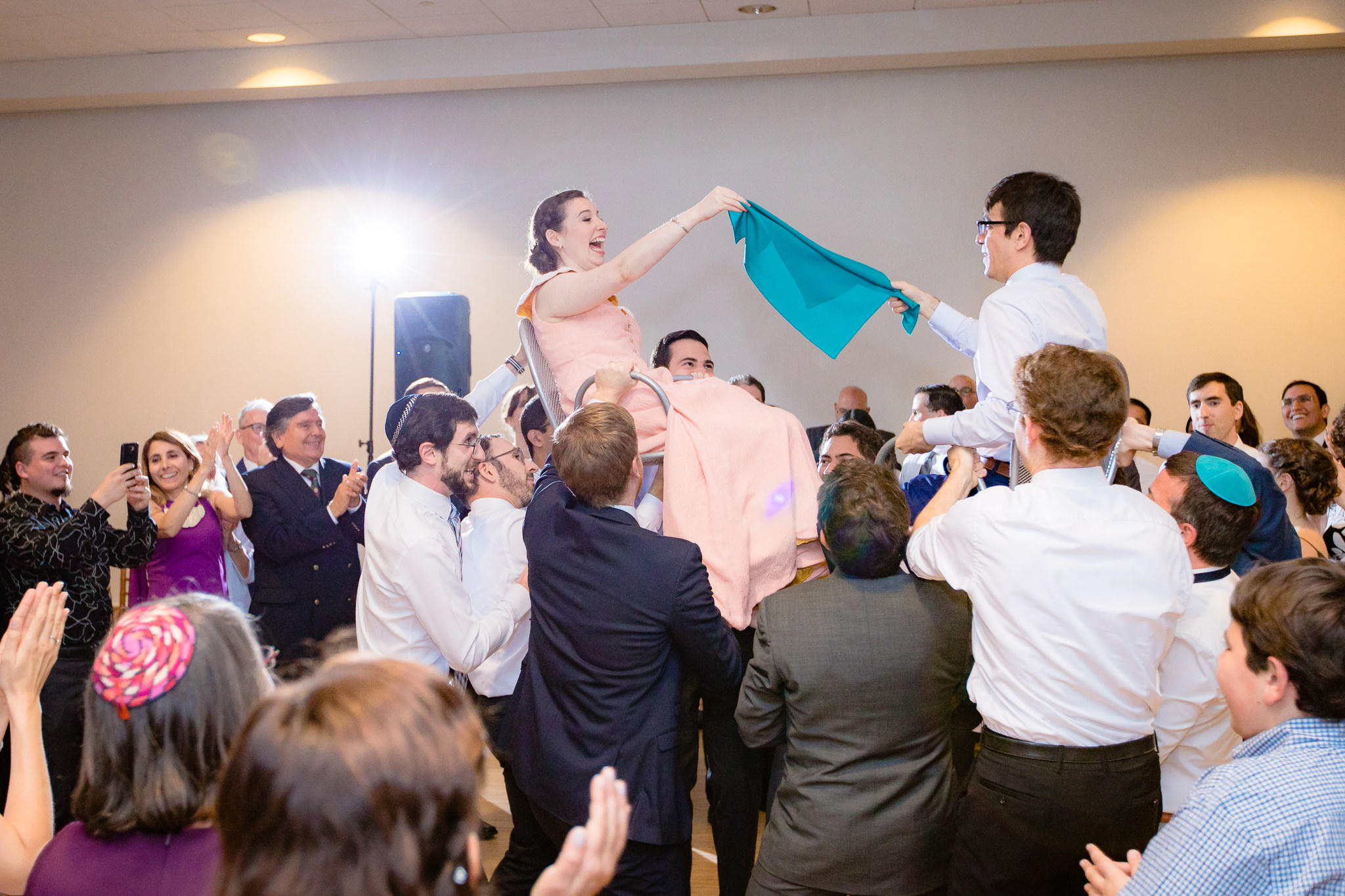 Guests lift newlyweds up on chairs during the hora at a Phipps Conservatory Jewish wedding reception