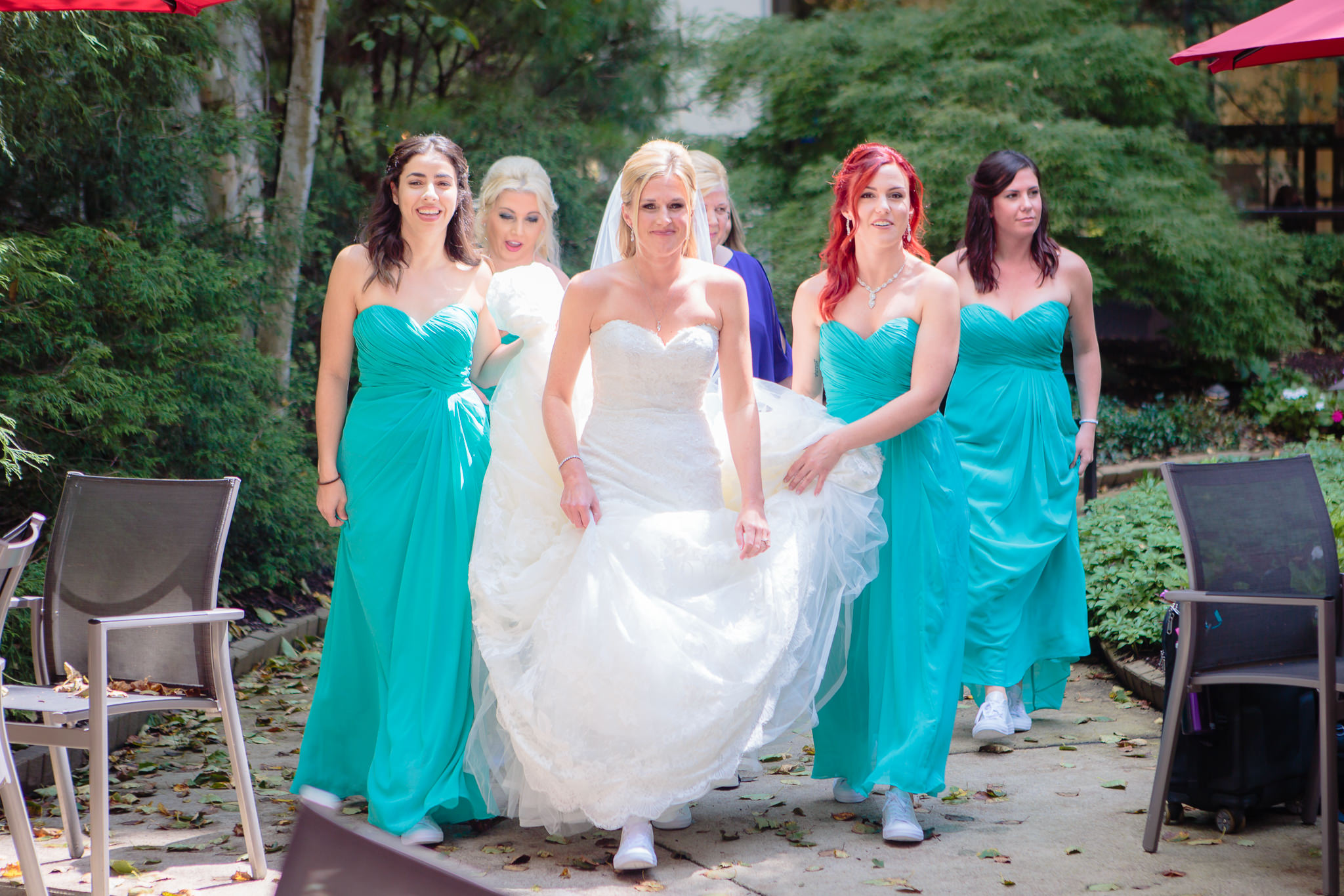 Bridesmaids help the bride walk to her first look in the Pittsburgh Airport Marriott courtyard