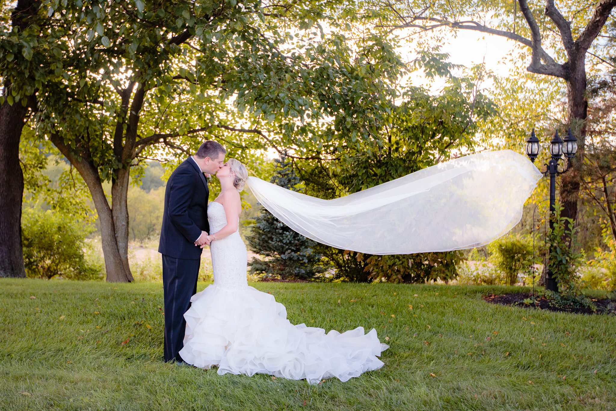 Groom kisses bride as her cathedral veil blows in the wind at Greystone Fields