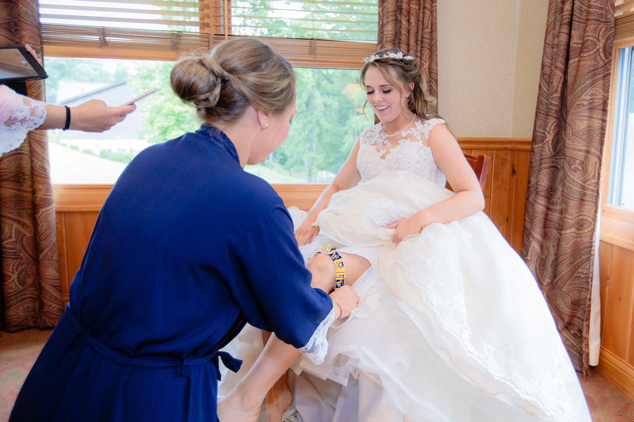 Bridesmaid puts a Pittsburgh Penguins garter on the bride's leg before her Oglebay wedding