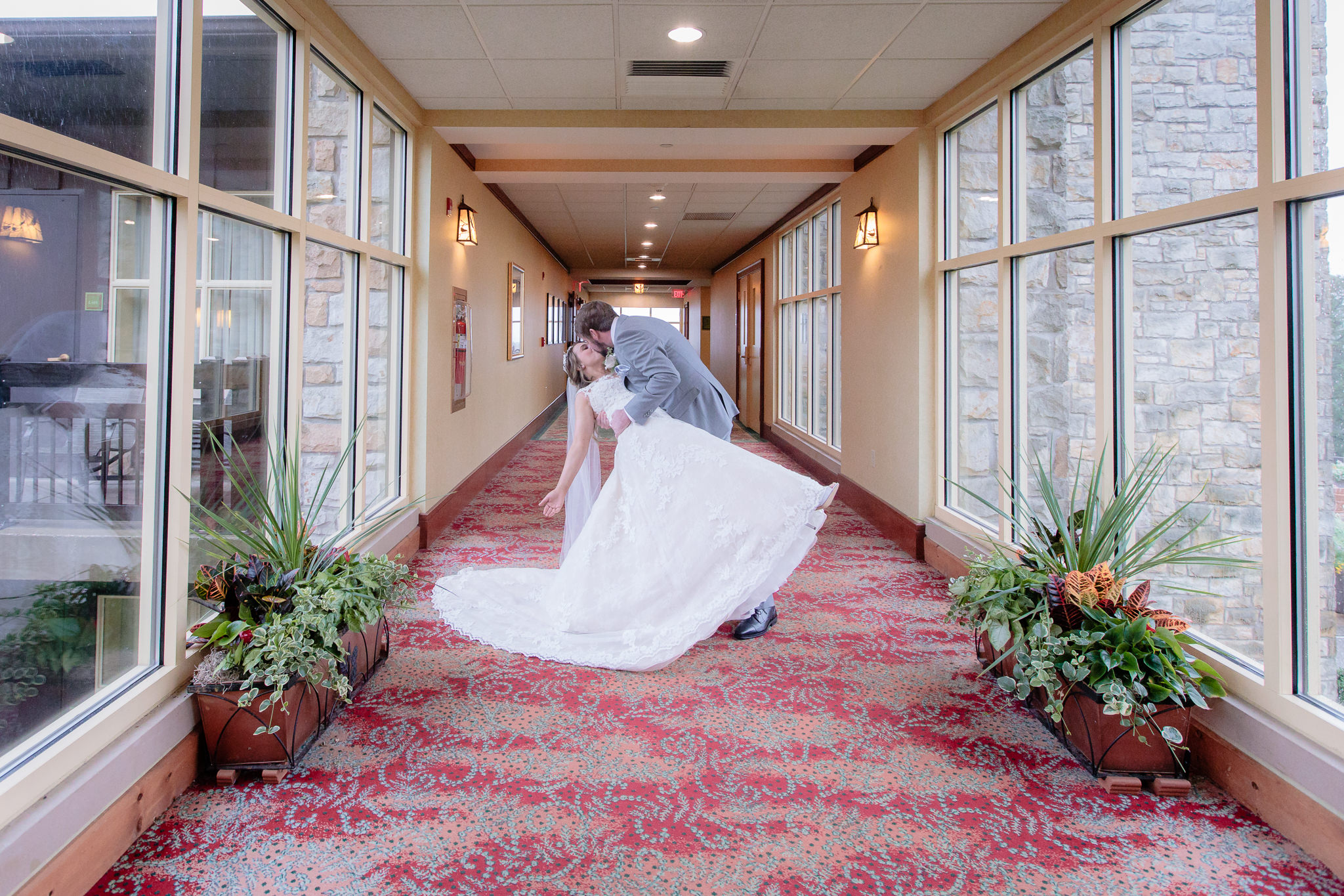 Groom dips his bride in a windowed corridor of Wilson Lodge at Oglebay