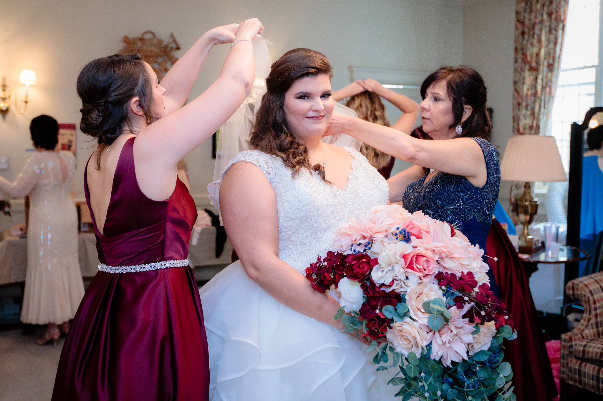 The bride poses with her DIY artificial flowers as a bridesmaid helps adjust her veil at Mt. Lebanon United Methodist Church
