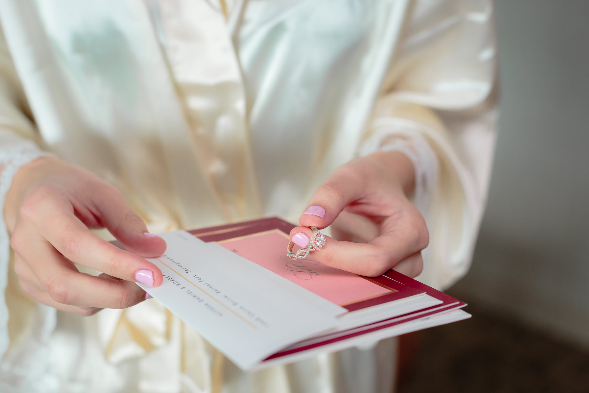 Bride holds her invitation and gold engagement ring in her hands
