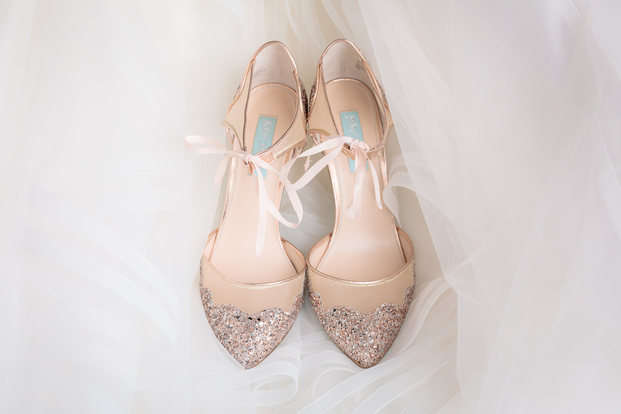 Bride's gold glitter wedding shoes rest on the white tulle skirt of her Allure bridal gown