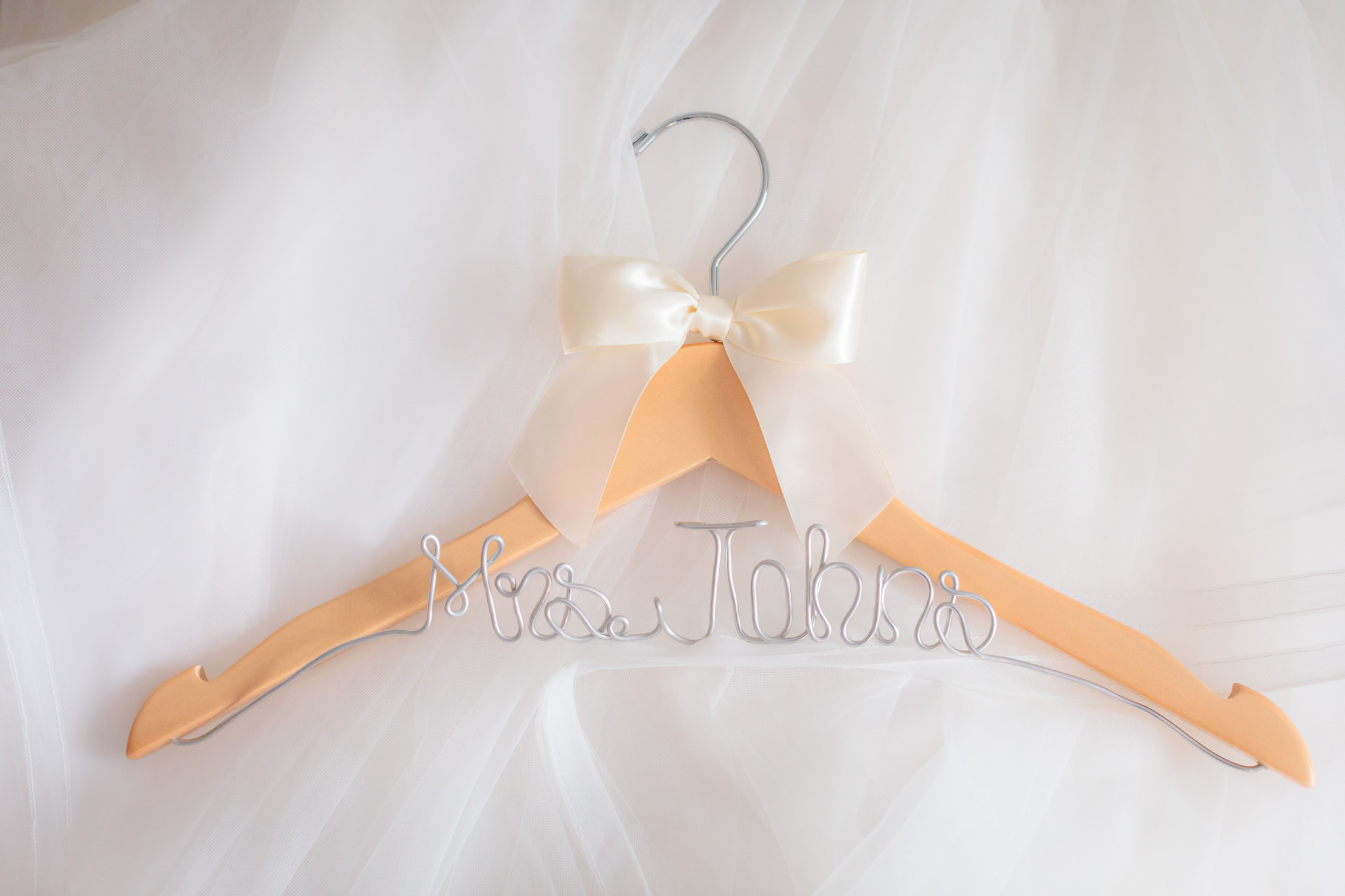 Custom hanger for the bride's gown rests on her white tulle skirt