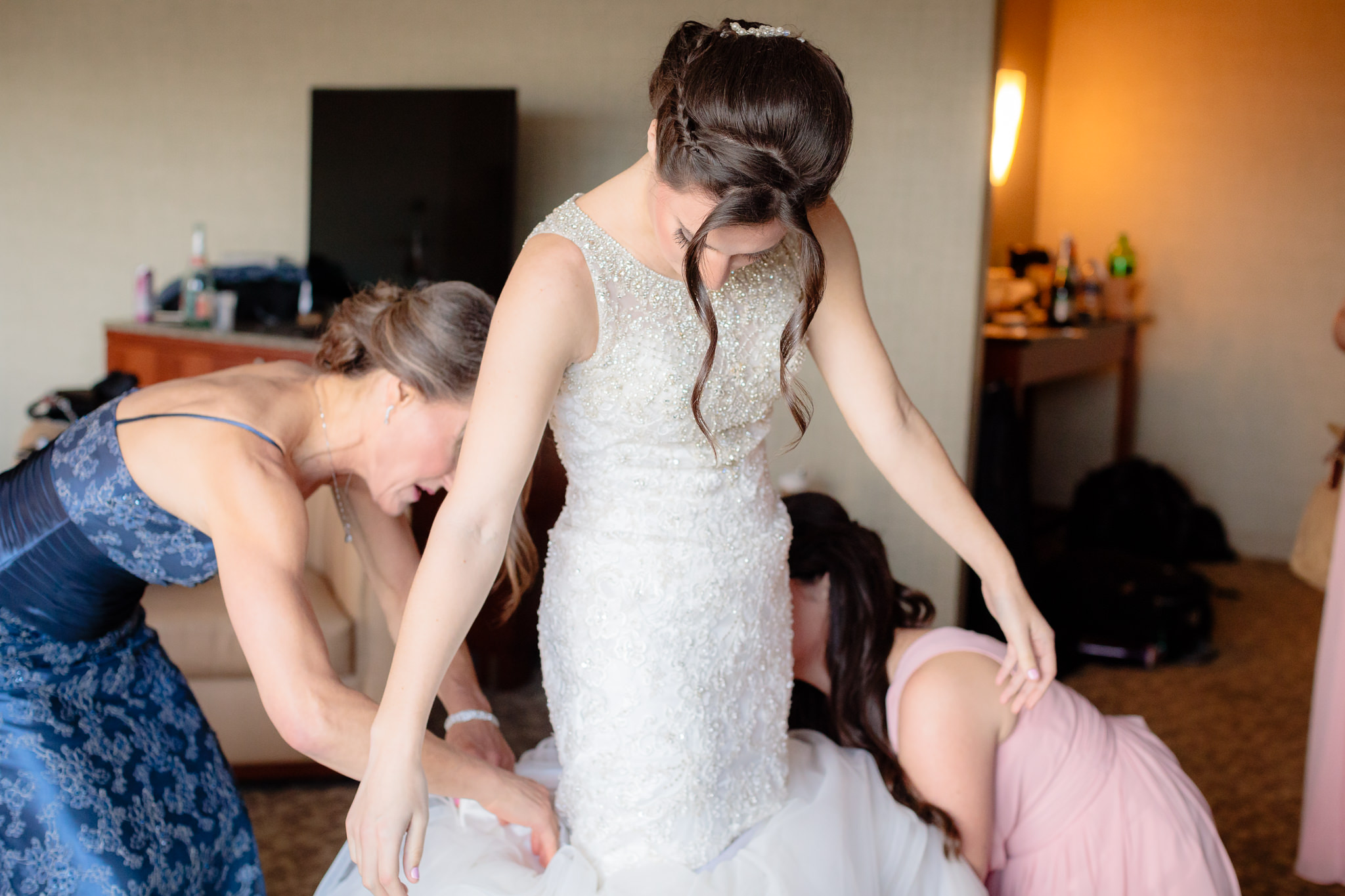 Mother of the bride and a bridesmaid help her into her Allure wedding dress