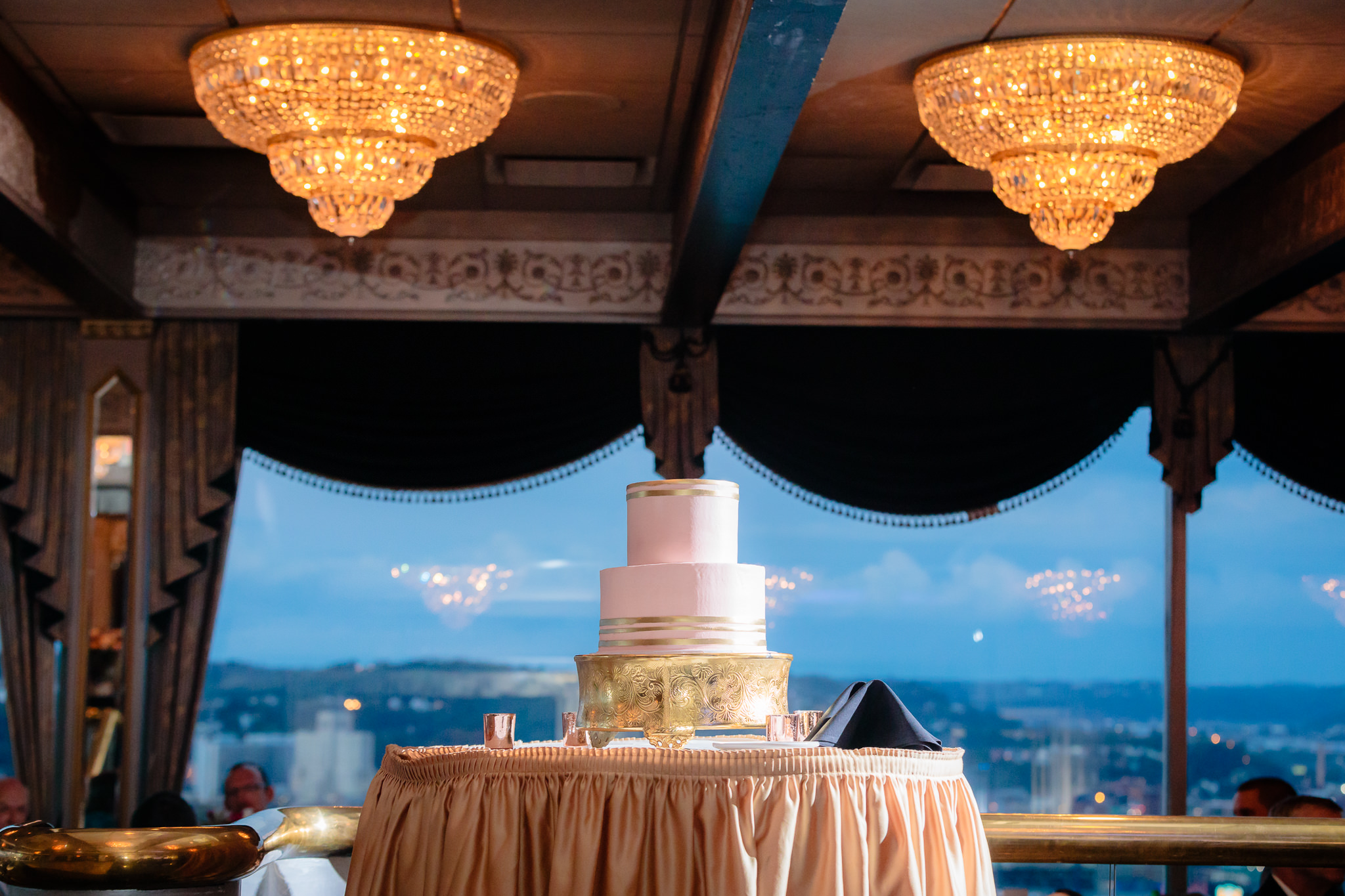 Wedding cake by Oakmont Bakery sits under crystal chandeliers at the LeMont