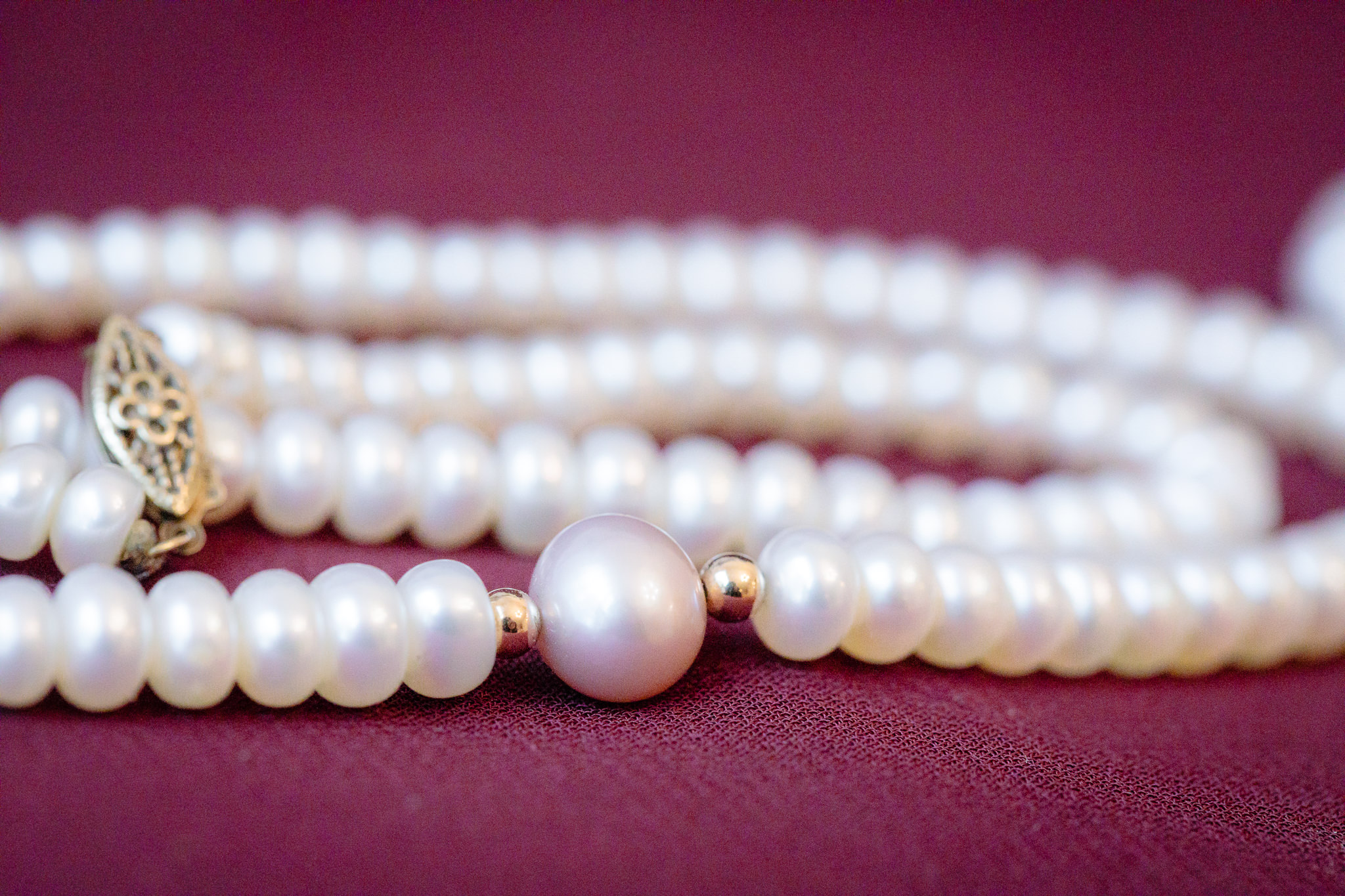 Bride's white pearl necklace rests on a burgundy bridesmaids dress
