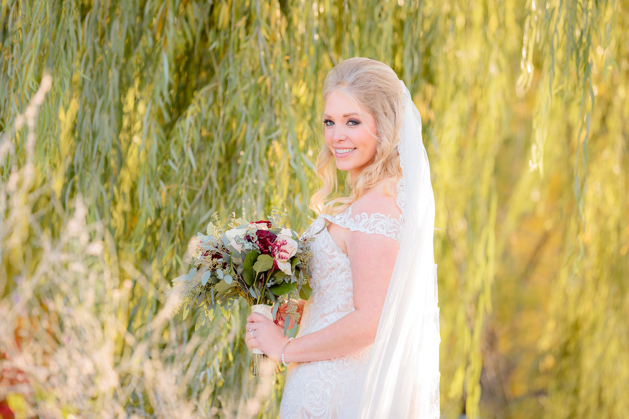 Bride smiles in front of a willow tree at Riverside Landing in Oakmont