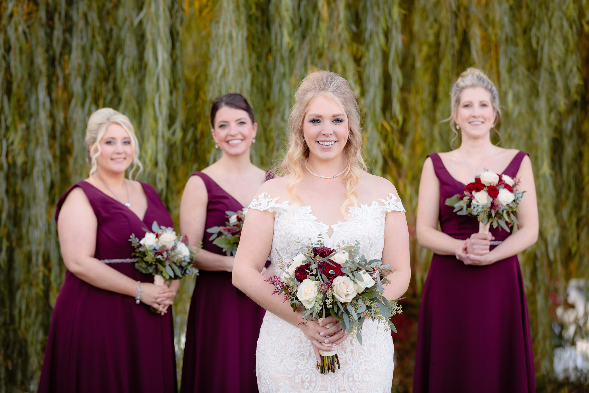 Bride with her bridesmaids in front of a willow tree at Riverside Landing in Oakmont, PA