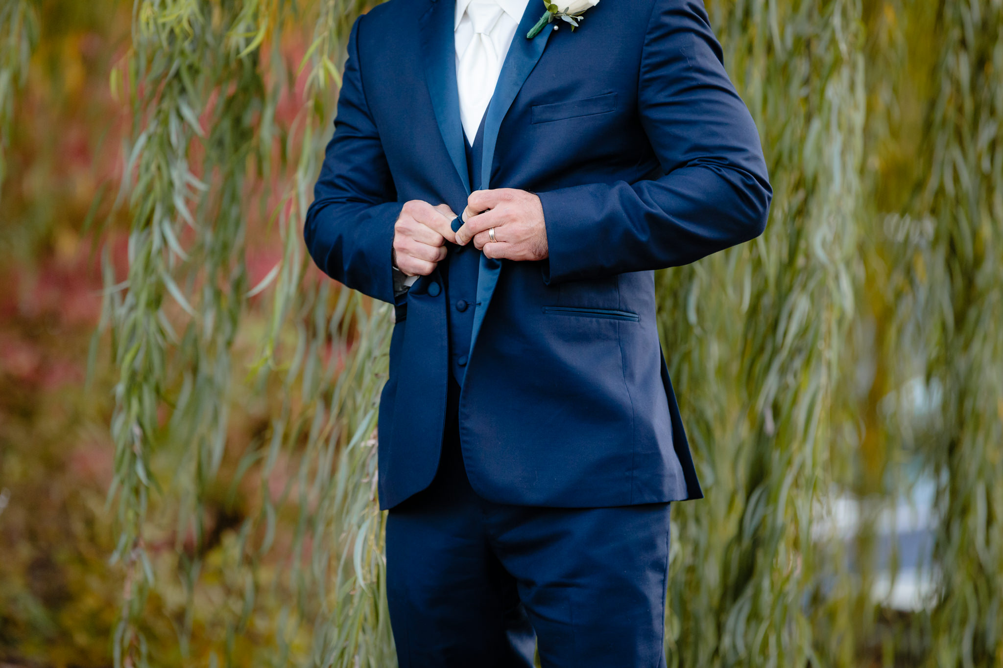 Groom buttons his navy tuxedo jacket before his Riverside Landing wedding