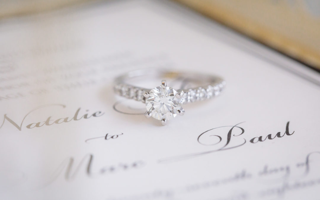 Solitary diamond engagement ring rests on a wedding invitation by Hello Beautiful Designs