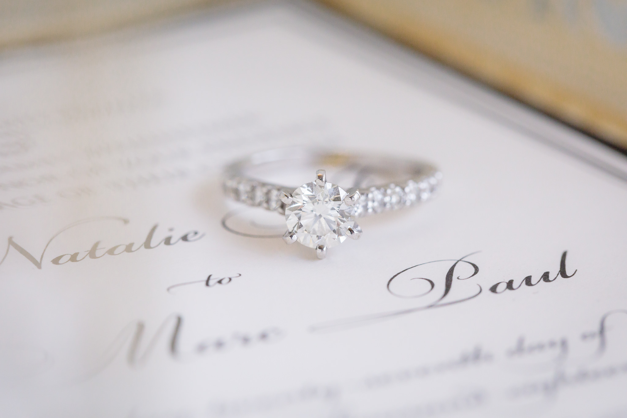 Solitary diamond engagement ring rests on a wedding invitation by Hello Beautiful Designs