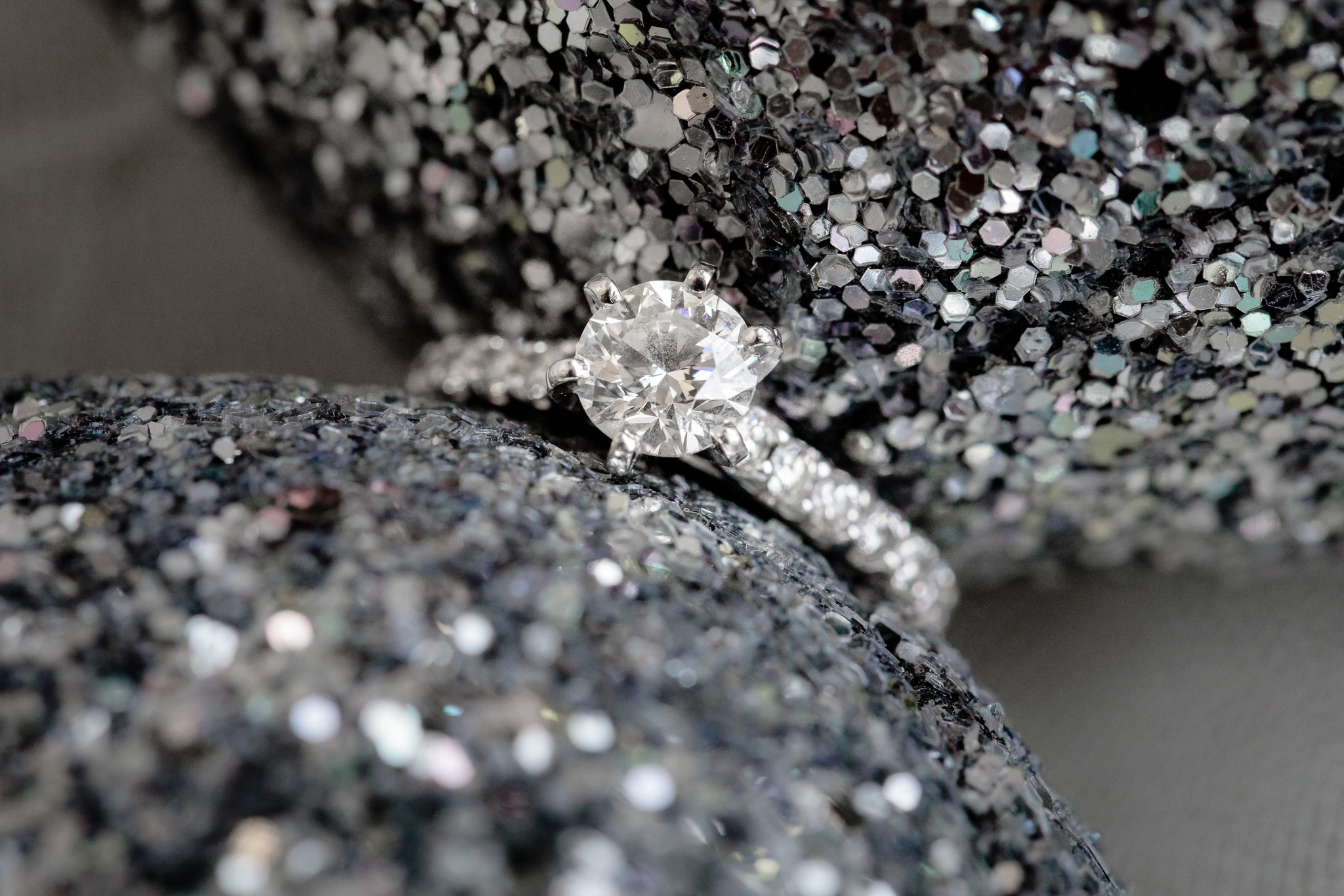 Diamond engagement ring rests between silver glitter shoes