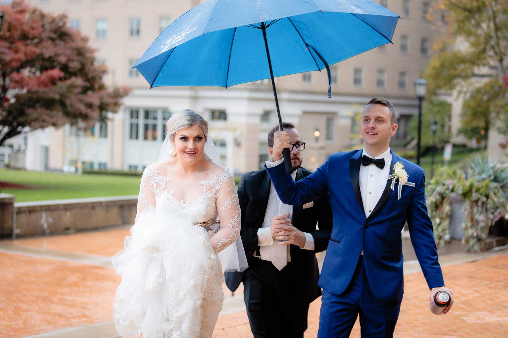 Groom holds an umbrella for the bride as they walk to Soldiers & Sailors