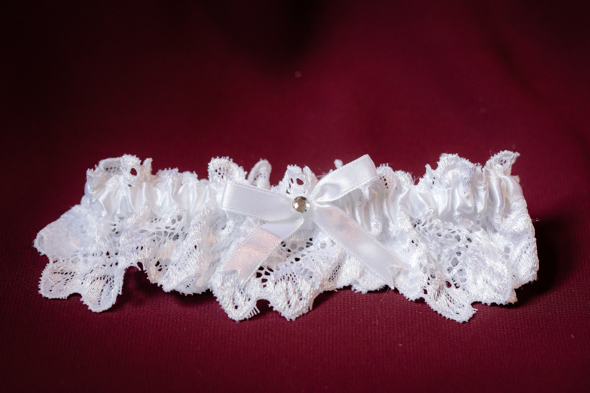 Bride's white lace garter rests on a burgundy bridesmaids gown