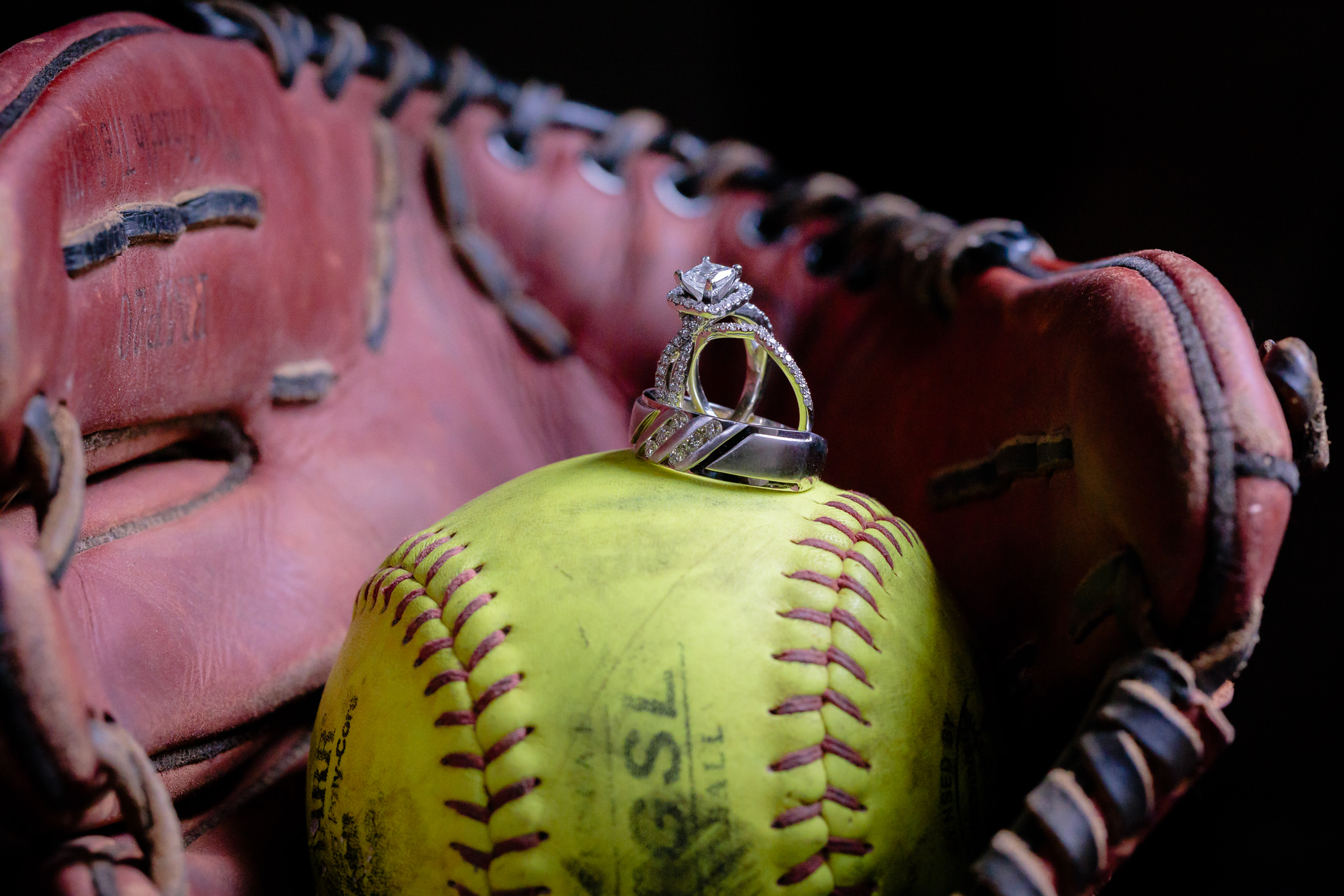 Wedding bands rest on a yellow softball inside a glove