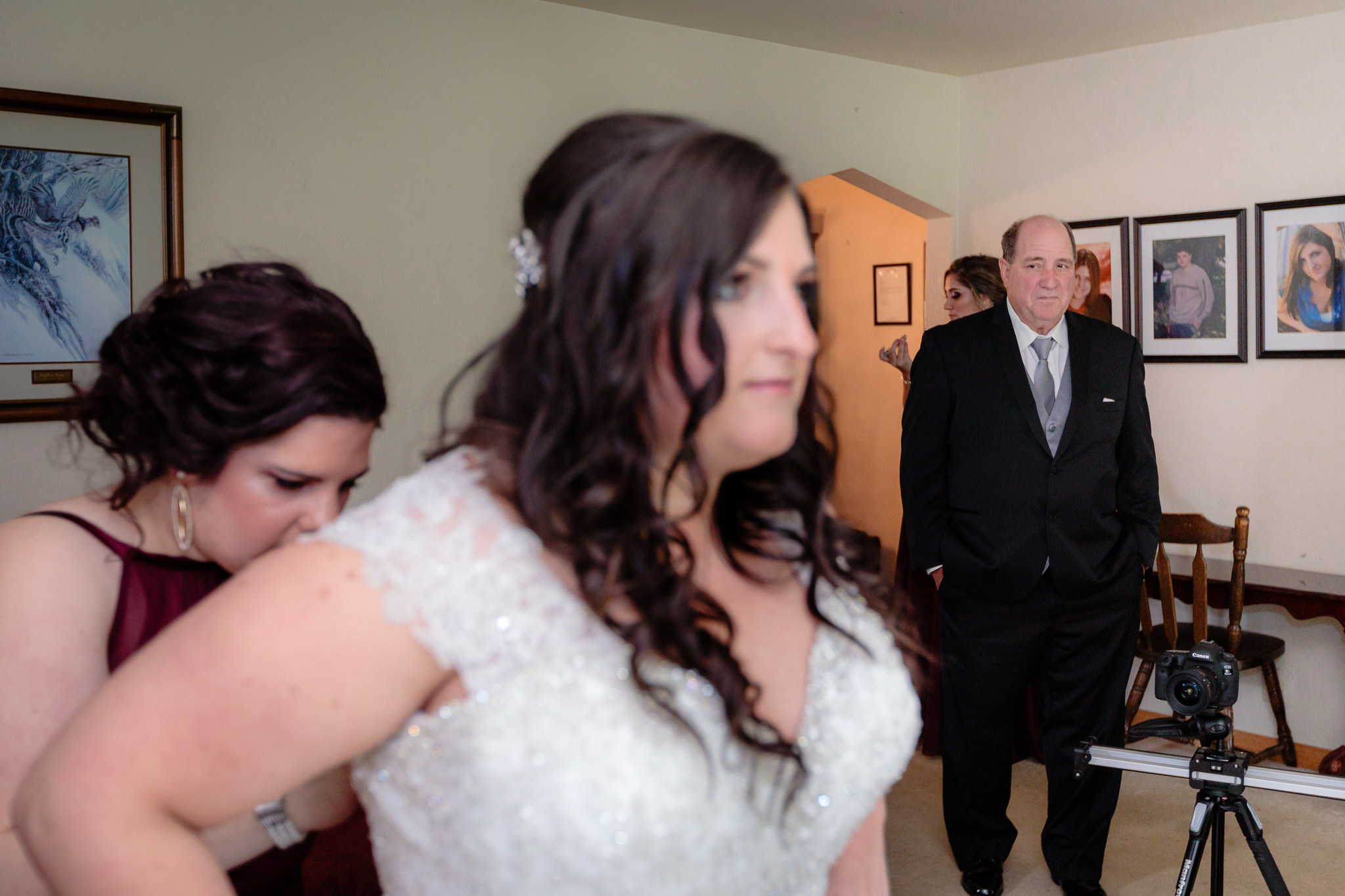 Father of the bride watches as her sister buttons the back of her Allure wedding dress