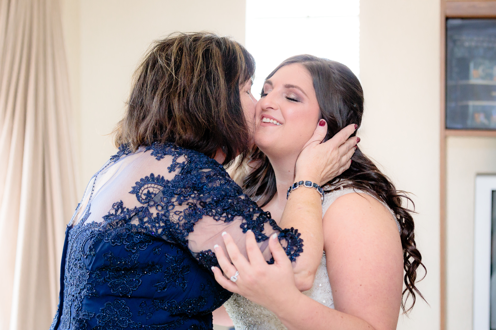 Mother of the bride kisses bride's cheek after seeing her in her wedding dress