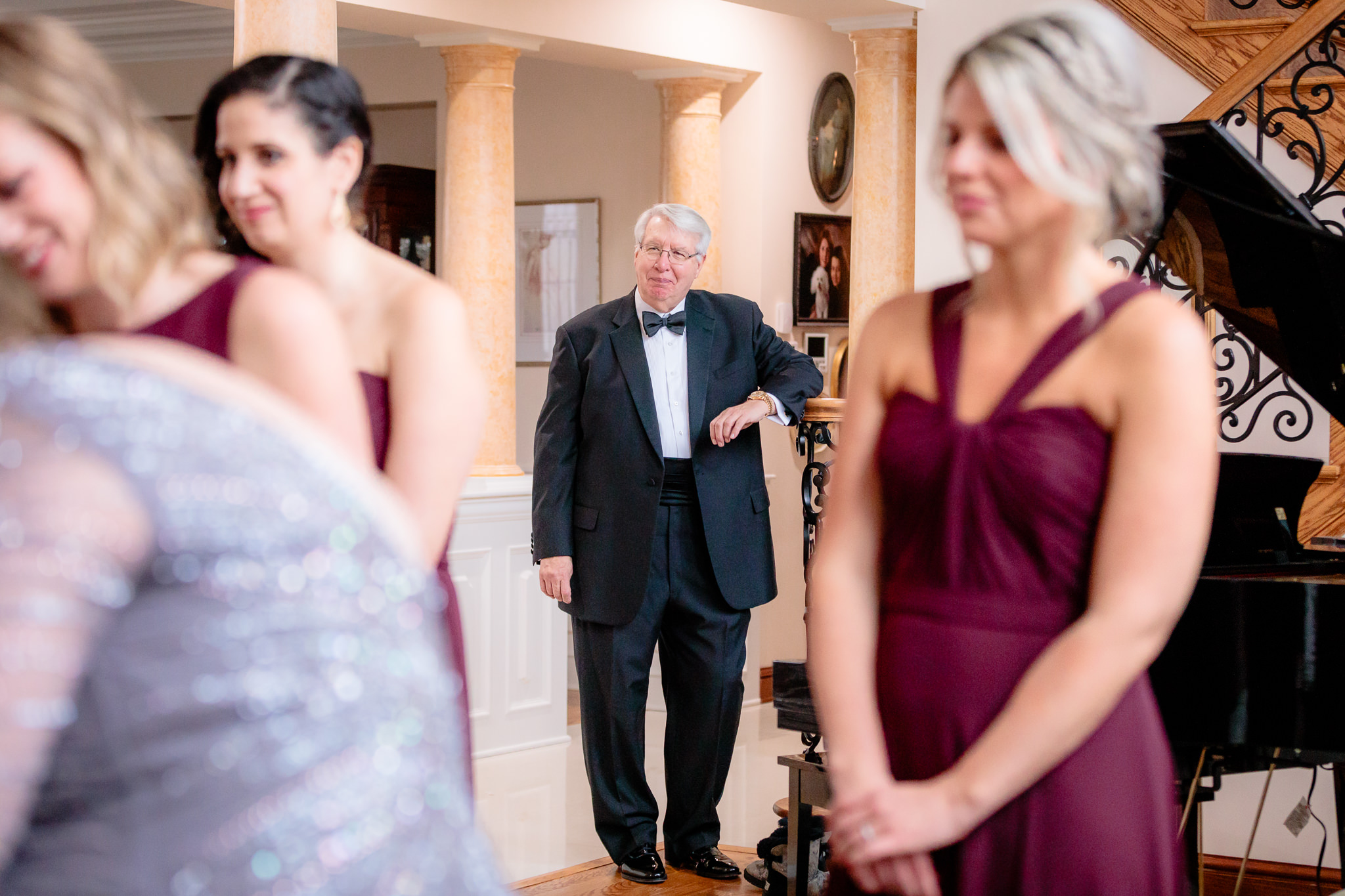 Father of the bride looks on as bridesmaids button her dress