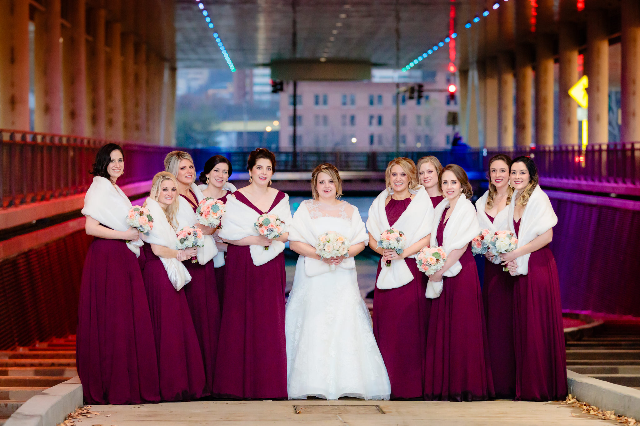 Bride with her bridesmaids in burgundy dresses and white fur shawls at the David L. Lawrence Convention Center