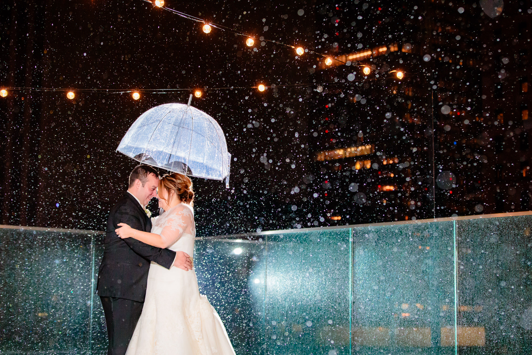 Newlyweds in the rain under a clear umbrella on the roof of Hotel Monaco Pittsburgh