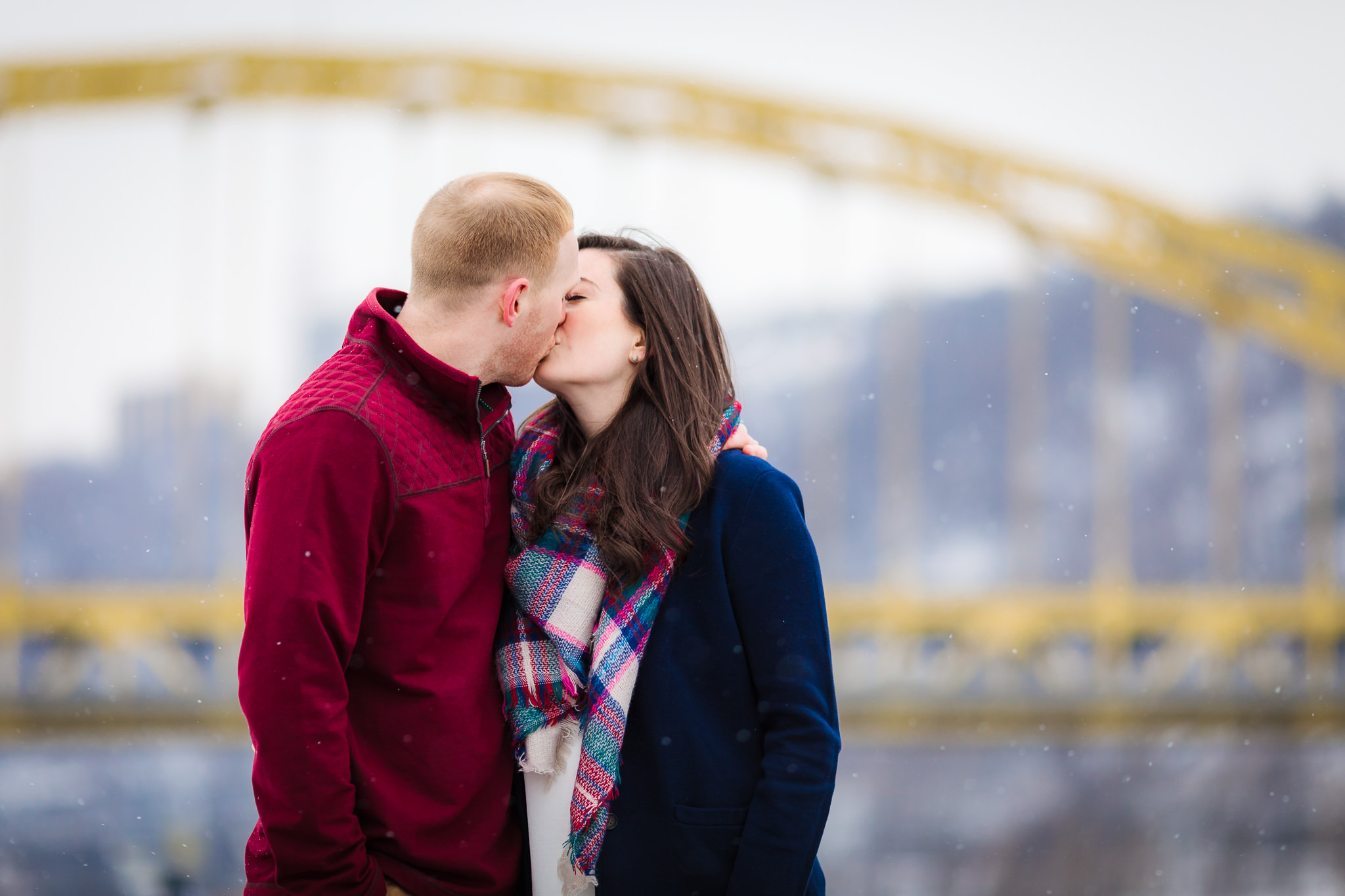 Engaged couple kisses in front of Fort Pitt Bridge at Point State Park