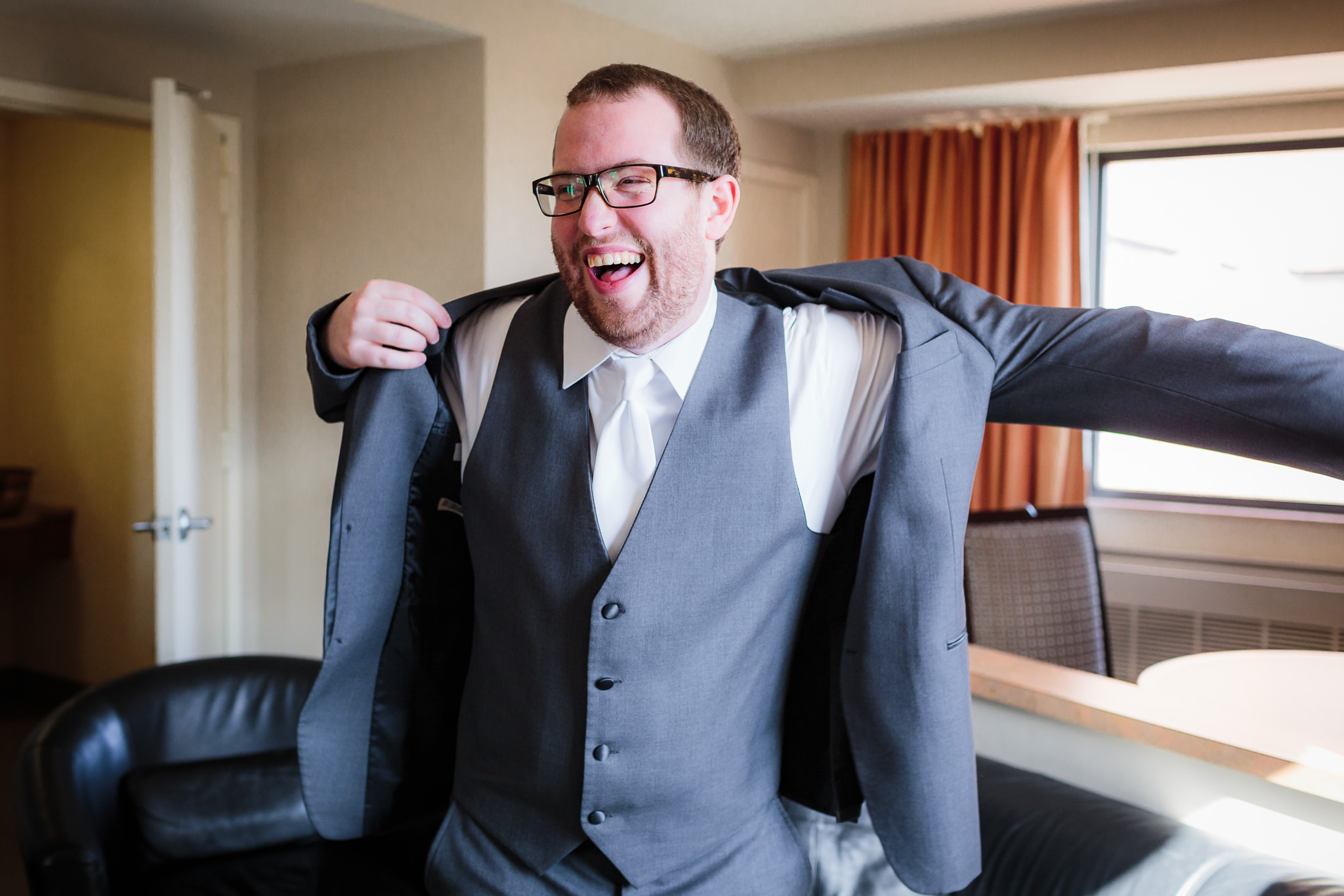 Groom laughs as he puts on his gray Joseph Abboud tux jacket from Men's Wearhouse