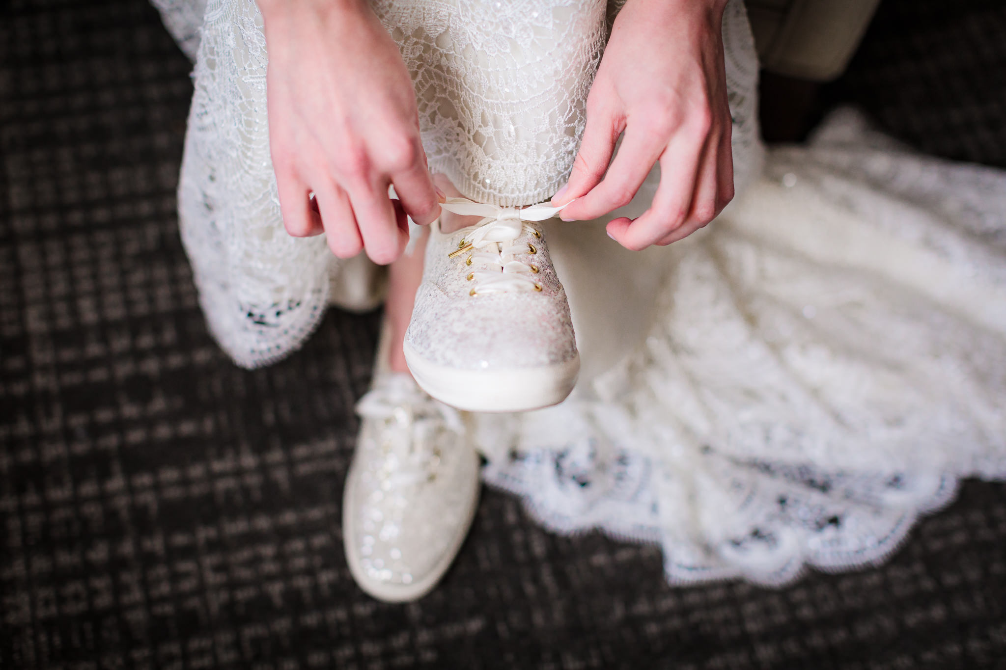 Bride ties the laces of her white sequence Kate Spade wedding shoes at the DoubleTree Pittsburgh Downtown