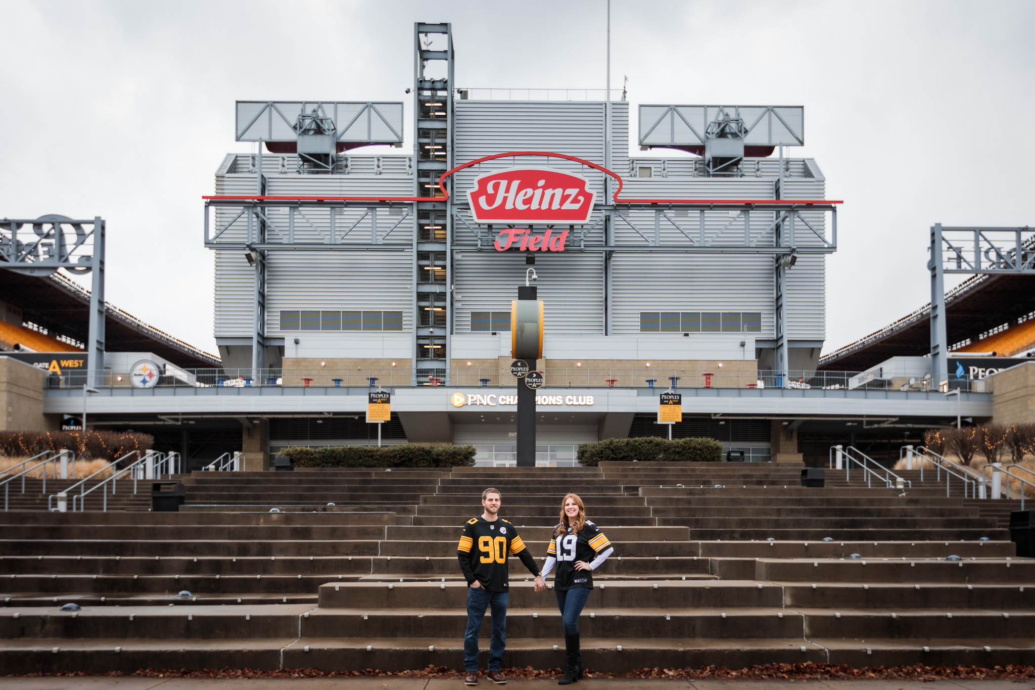 Engaged couple wearing Steelers jerseys holding hands in front of Heinz Field in Pittsburgh, PA
