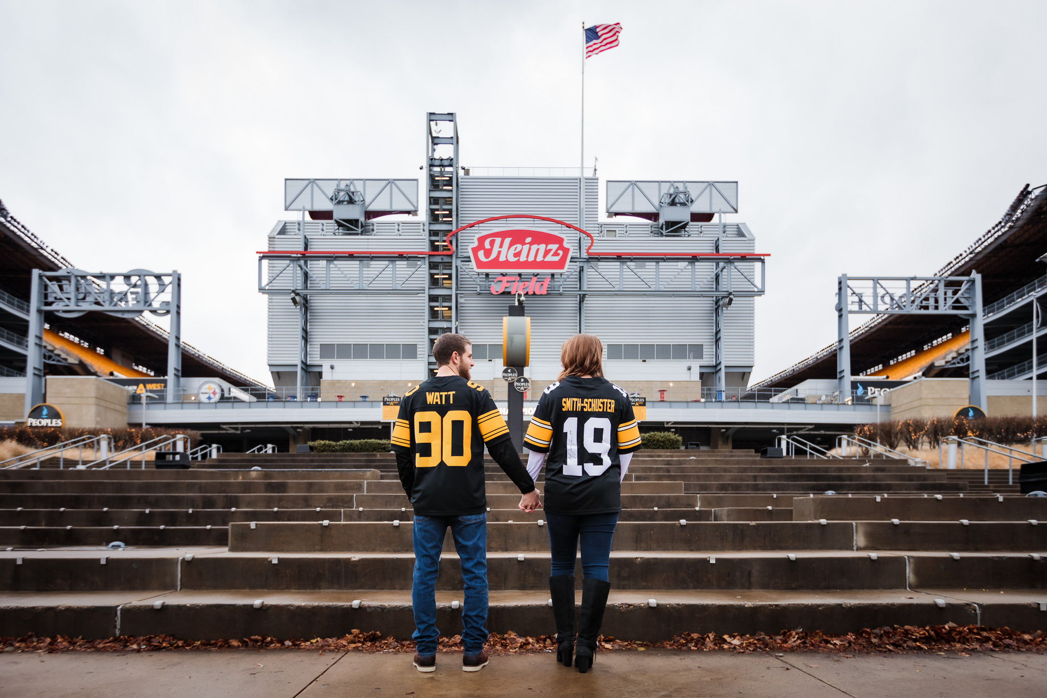 Engaged couple wearing Watt and Smith-Schuster Steelers jerseys in front of Heinz Field in Pittsburgh, PA