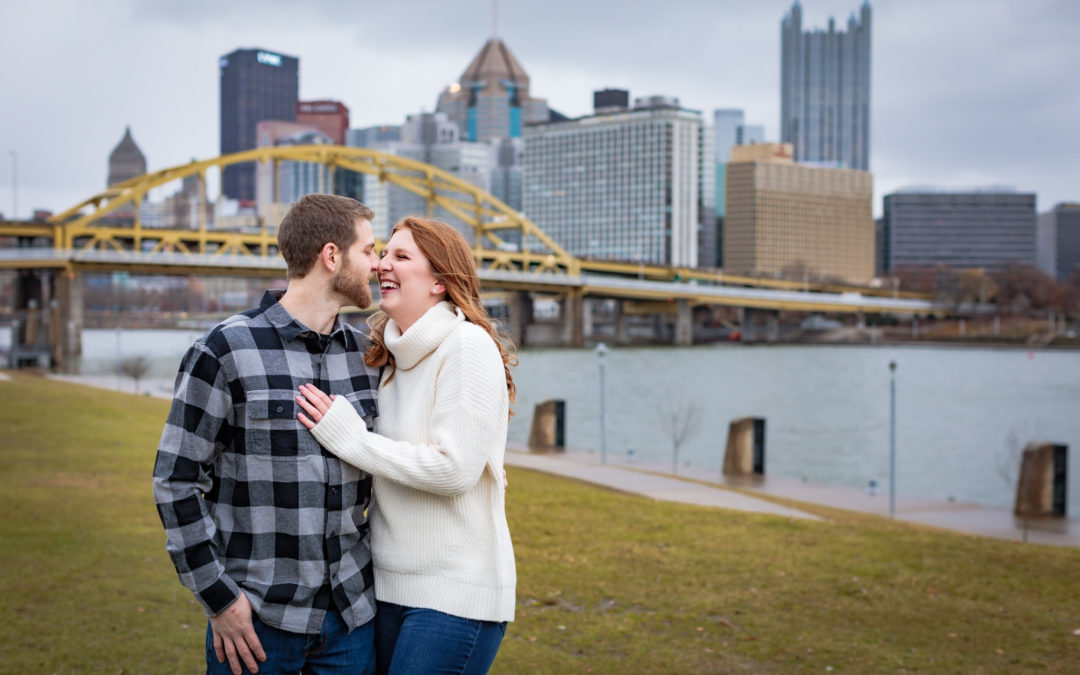 Couple laughs in front of Pittsburgh skyline during a North Shore engagement session