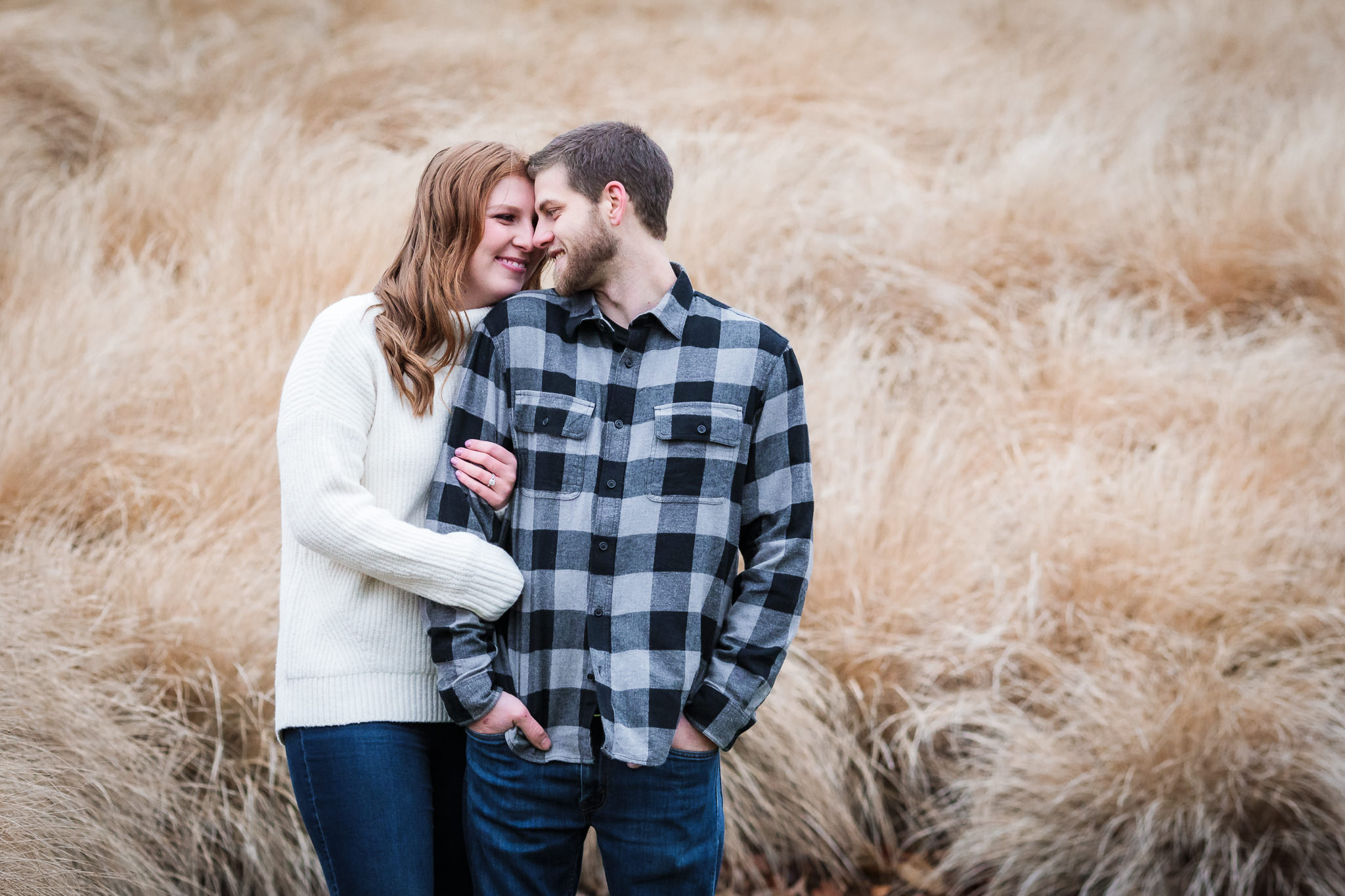 Couple nuzzles in front of tall grasses at a North Shore engagement session in Pittsburgh, PA