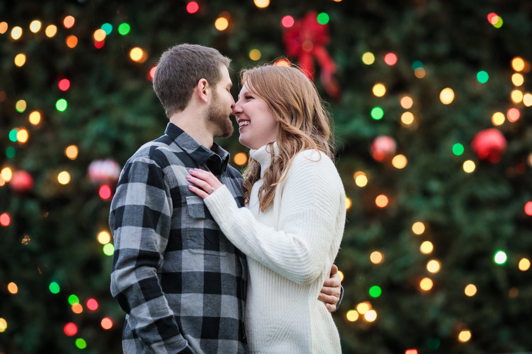 Couple nuzzles in front of a Christmas tree during a North Shore engagement session