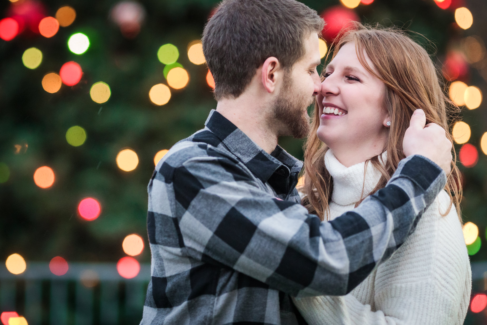 Couple laughs in front of Christmas tree lights at a North Shore engagement session in Pittsburgh, PA